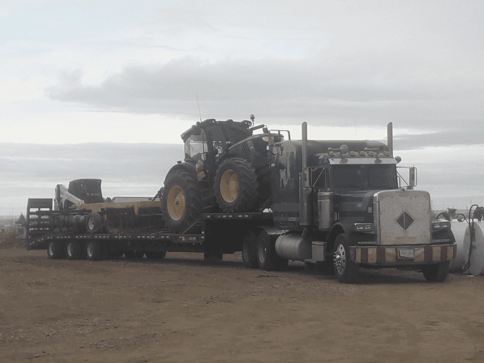 semi trailer hauling a green tractor and pieces of equipment